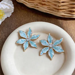 Close-up of light blue enamel flower earrings with zircon center on a white plate.