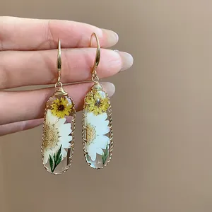 Dettaglio macro di orecchini a goccia in resina fatti a mano con fiori secchi naturali.