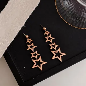 Detailed view of elegant rose gold tiered star-shaped dangling earrings on a black tray