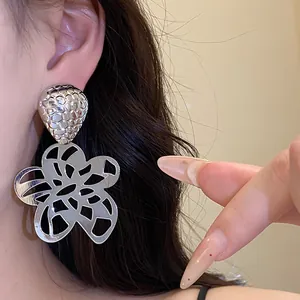 Detailansicht eines silbernen hohlen Blumenohrrings am Ohr eines weiblichen Models
