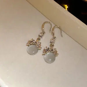 Detailed view of silver-tone hook earrings with shimmering rhinestones and round resin pendants.