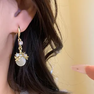 Close-up view of gold dangle earrings with white resin pendant and rhinestone accents