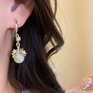 Detail shot of elegant diamond-studded gold hook earrings with white resin pendant