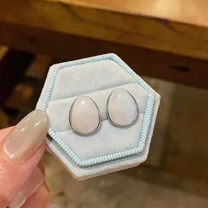Primo piano di eleganti orecchini a goccia in acrilico bianco in una scatola di velluto blu