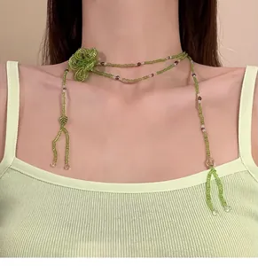 Dettaglio di una collana artigianale in perle di vetro verdi con fiore e nappa sul collo.