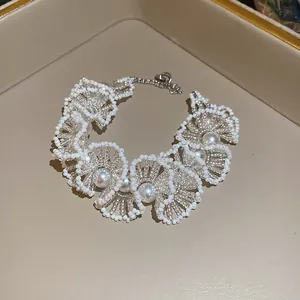 Close-up of delicate white beaded lace necklace with pearls on a beige background