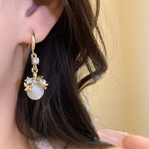 Detailed view of elegant gold drop earrings with white resin pendant and sparkling rhinestones.