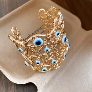 Dettaglio macro del bracciale rigido traforato dorato con diversi ciondoli Evil Eye