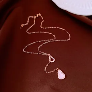Vergoldete Halskette mit Zirkonia-Herz und Flaschenkürbis-Anhänger auf braunem Stoff.