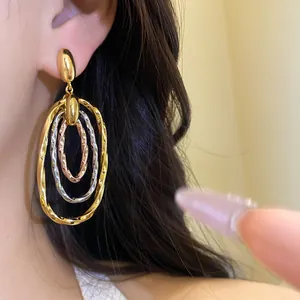 Detalle de primer plano de elegantes pendientes de aro ovalados retorcidos tricolores en la oreja