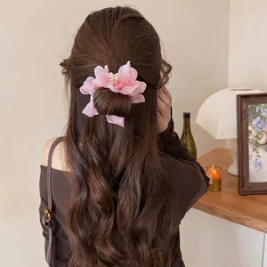 Elegant pink chiffon flower hair scrunchie with pearl detail shown on long wavy hair.