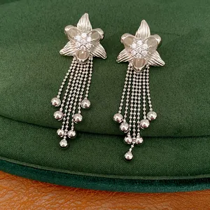 Detail shot of silver flower tassel earrings with clear CZ stones on green velvet cushion