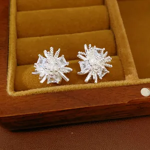 Gros plan de boucles d'oreilles fleurs en argent avec zircons dans un écrin en bois.