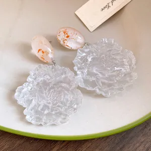 Macro detail of transparent resin flower earrings featuring delicate gold foil flakes
