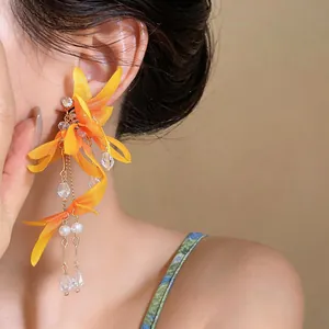 Macro detail of yellow fabric flower earrings featuring long crystal and pearl tassels.