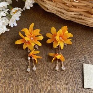 Detailed view of vibrant yellow fabric flower tassel earrings with pearls on rustic wood