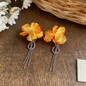Detail of orange fabric flower earrings with sparkling zirconia and long tassels