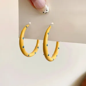 A detailed view of stylish yellow enamel hoop earrings with blue polka dots design.