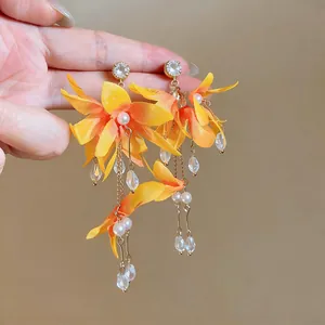 Detailed shot of orange fabric flower earrings with sparkling rhinestones and tassels.