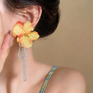 Close-up view of elegant orange fabric flower earrings with sparkling rhinestone tassels