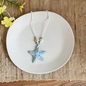 Blue ceramic starfish necklace with white cord on a minimalist plate.