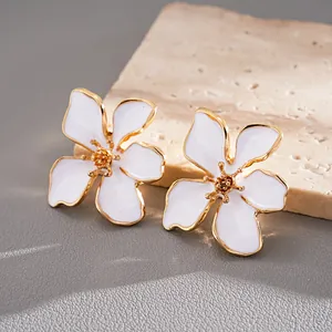 Primer plano de elegantes pendientes de flor de esmalte blanco con estambres y bordes dorados