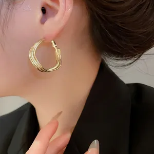 Gros plan montrant les détails de boucles d'oreilles créoles dorées à trois couches ondulées