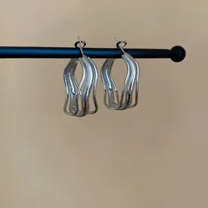 Gros plan de boucles d'oreilles créoles argentées minimalistes à triple vague irrégulière
