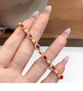 Gros plan détaillé d'un bracelet en or vintage avec des zircons rouges sur une main.