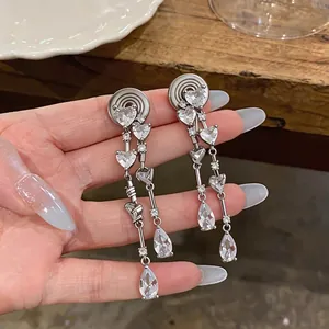 Élégants clips d'oreilles avec zircons en cœur et goutte tenus sur du bois