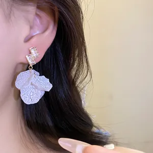 Close-up of elegant petal drop earrings with sparkling zircon studs worn on ear.