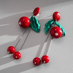 Macro detail shot of red cherry resin earrings with green leaves and silver chain tassels