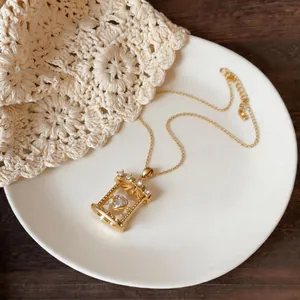 Detail of dainty golden cage pendant necklace featuring a sparkling heart-shaped zircon