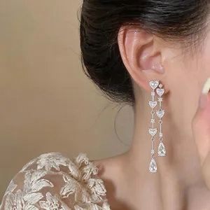 Gros plan de boucles d'oreilles élégantes en zircon avec cœurs et glands portées.