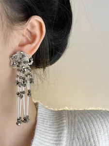 Detail view of elegant silver flower-shaped beaded tassel earrings worn on model's ear