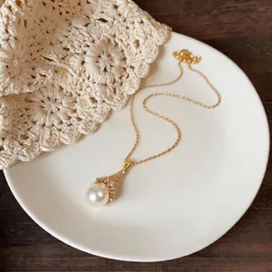 Close-up of an elegant gold zircon fan pendant featuring a round white pearl on a plate