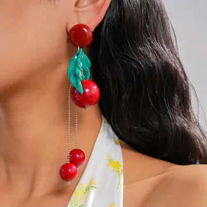 Detail showing red resin cherry fringe earrings with green leaves on model's ear