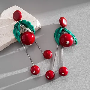 Close-up detail of red cherry resin earrings with green leaves and silver tassels