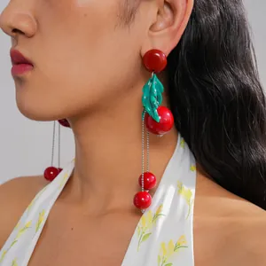 Detailed view of red resin cherry tassel earrings with green leaves worn by a model