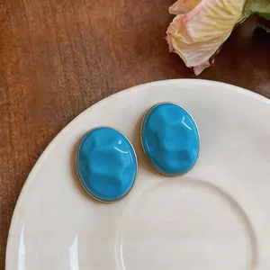 Macro view of oval blue earrings featuring ripple textures and elegant golden frames.
