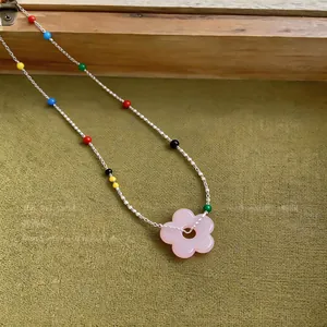 Close-up view of a pink flower pendant necklace with colorful beads on a silver chain.