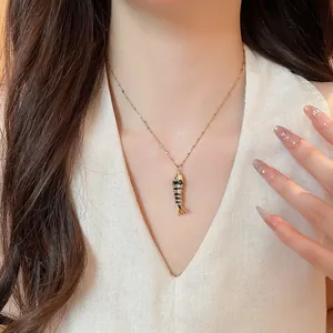 Detail view of a gold and black enamel fish skeleton pendant necklace on a model.