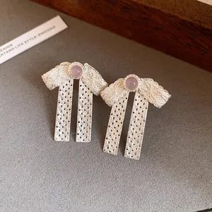 Detail view of elegant silver bowknot stud earrings with lace texture and purple stone.