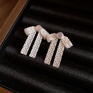 Close-up detail of silver bow-knot pendant earrings with pink gemstone on black velvet