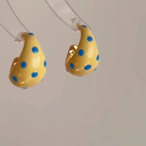 Detail view of yellow C-shaped enamel earrings with blue polka dots on display stand