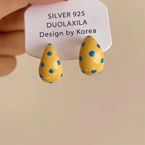 Close-up of yellow drip oil drop earrings with blue polka dots on a display card