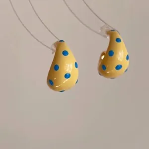 Detailed close-up view of yellow enamel C-shape hoop earrings with blue polka dots pattern