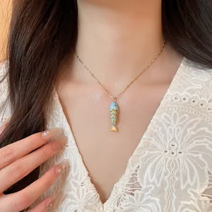 Detailed shot of a dainty gold necklace with a colorful enamel fish pendant on model.