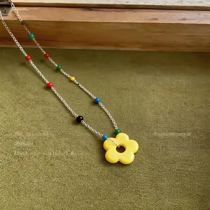 Close-up detail of a vibrant colorful beaded necklace featuring a bright yellow flower pendant