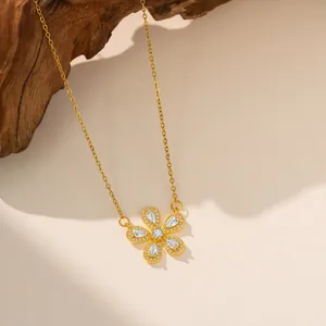 Primer plano de un collar con colgante de flor dorada y piedras de circón sobre fondo de madera.